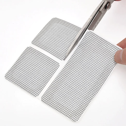 Hand cutting adhesive window screen repair patches with scissors on white background
