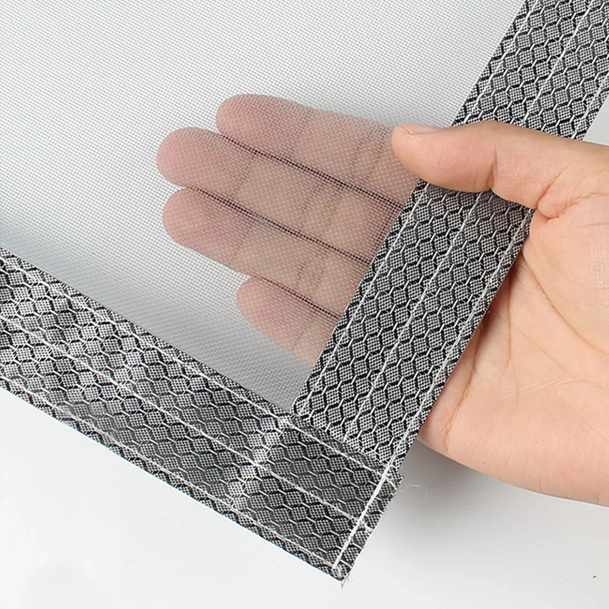 Hand holding reinforced mesh screen door with hexagonal patterned edge stitching